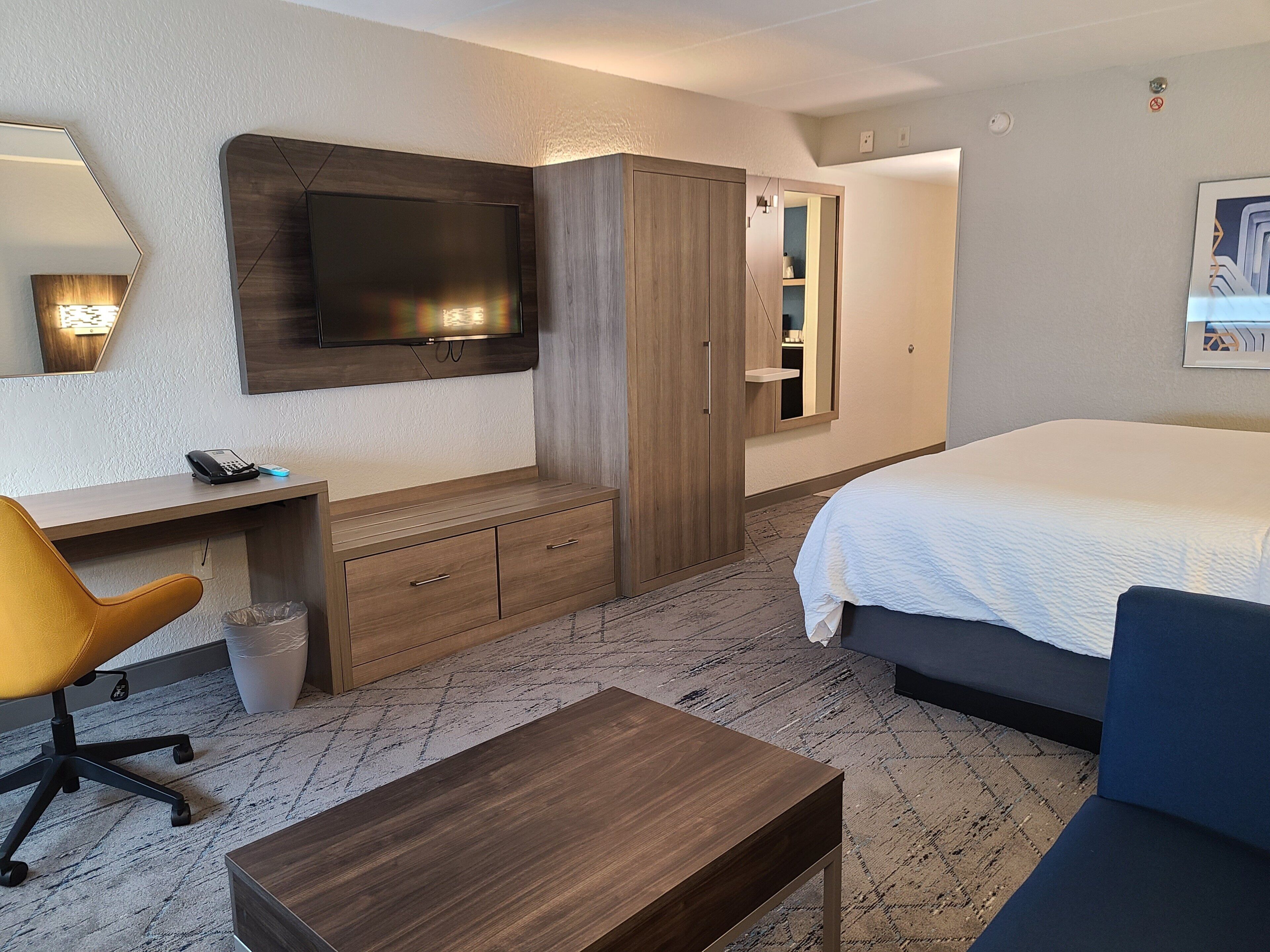 A hotel room with a bed, a desk, a chair, a wardrobe, and a television.