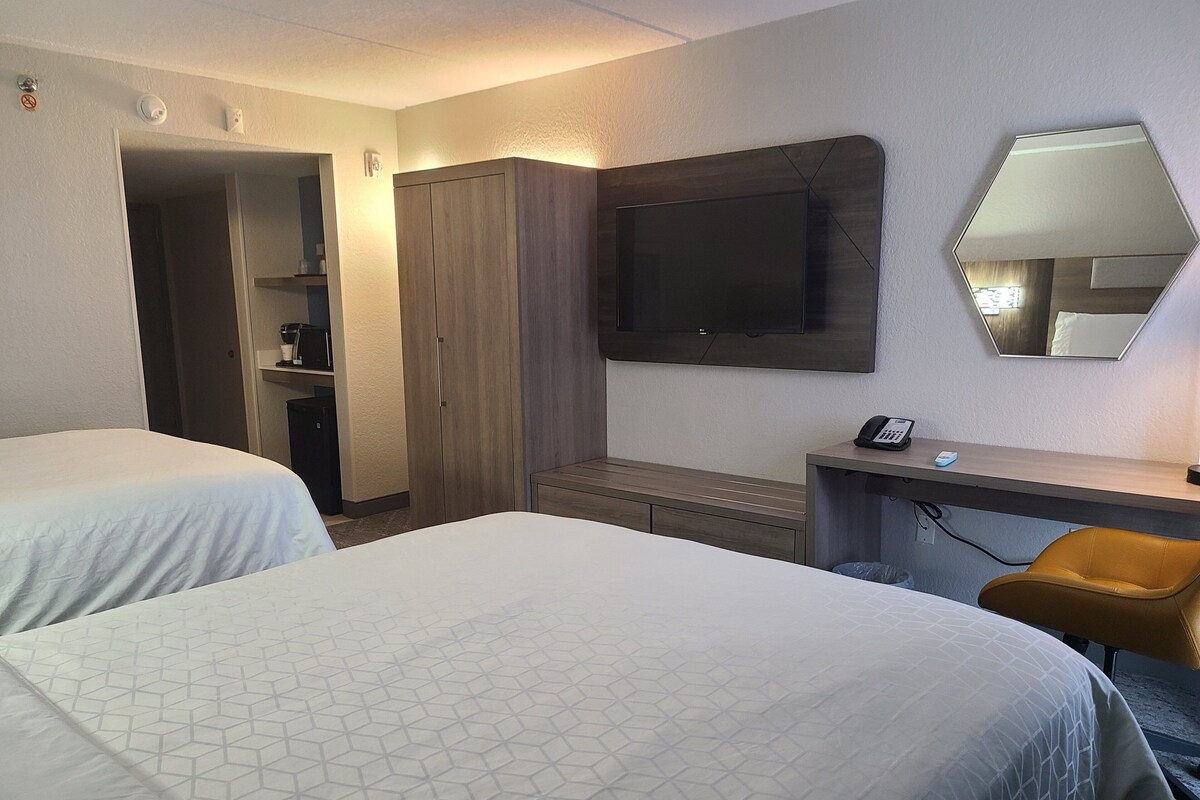 Habitación de hotel con dos camas, un escritorio, una silla, un armario y un televisor.