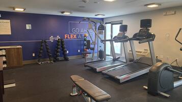 A gym with a treadmill, weight machines, and dumbbells.