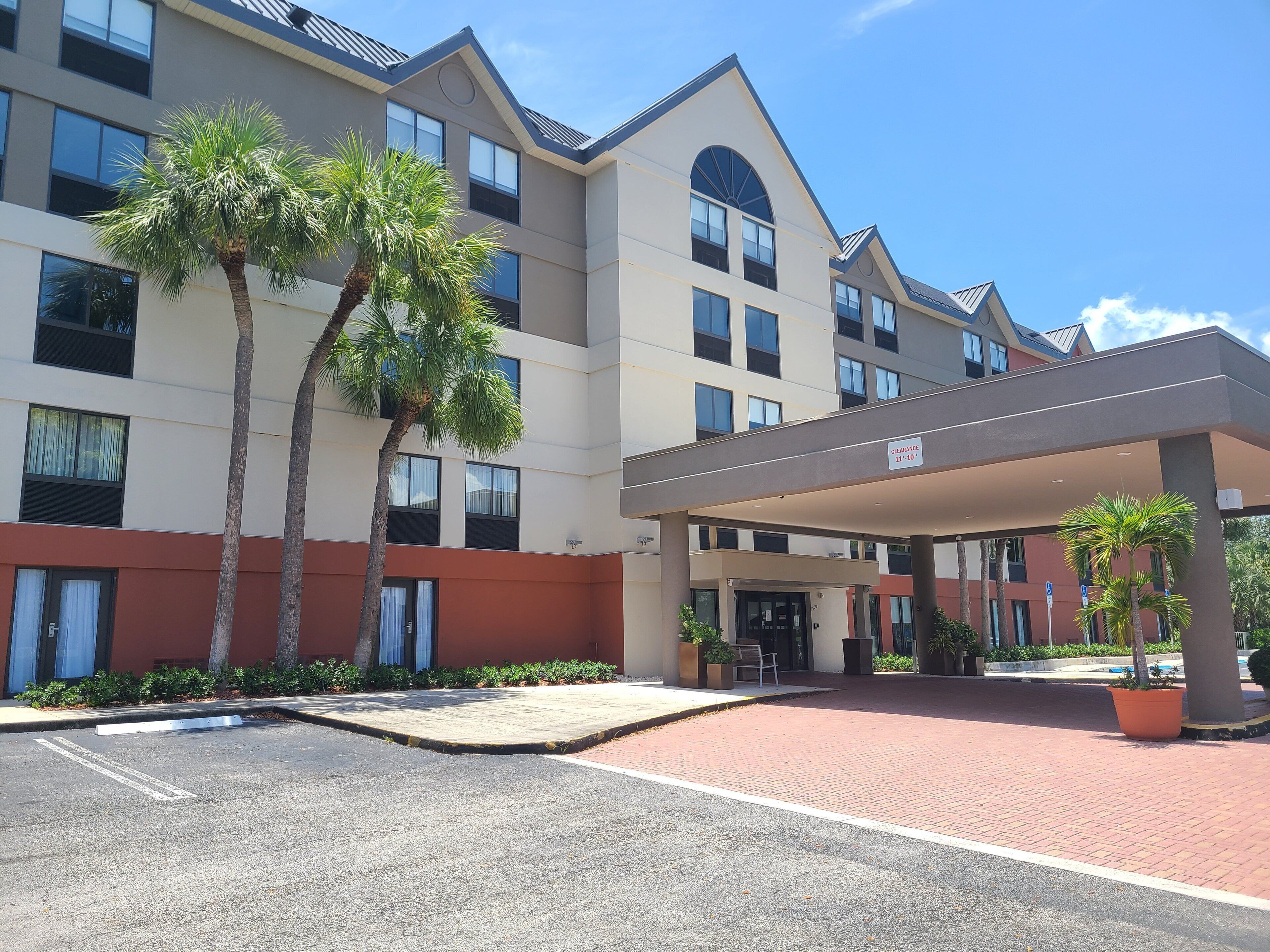 A hotel with a covered entrance, palm trees, and a parking lot.