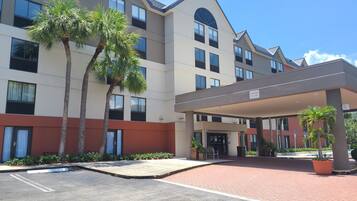 A hotel with a covered entrance, palm trees, and a parking lot.