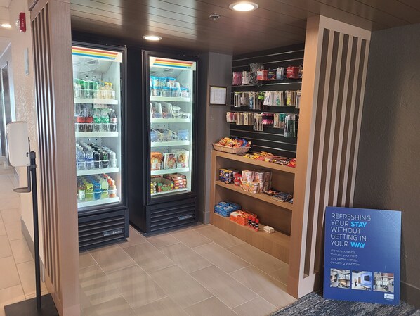 Vestíbulo de hotel con dos dispensadores de bebidas, un bar de aperitivos y un letrero sobre renovaciones.