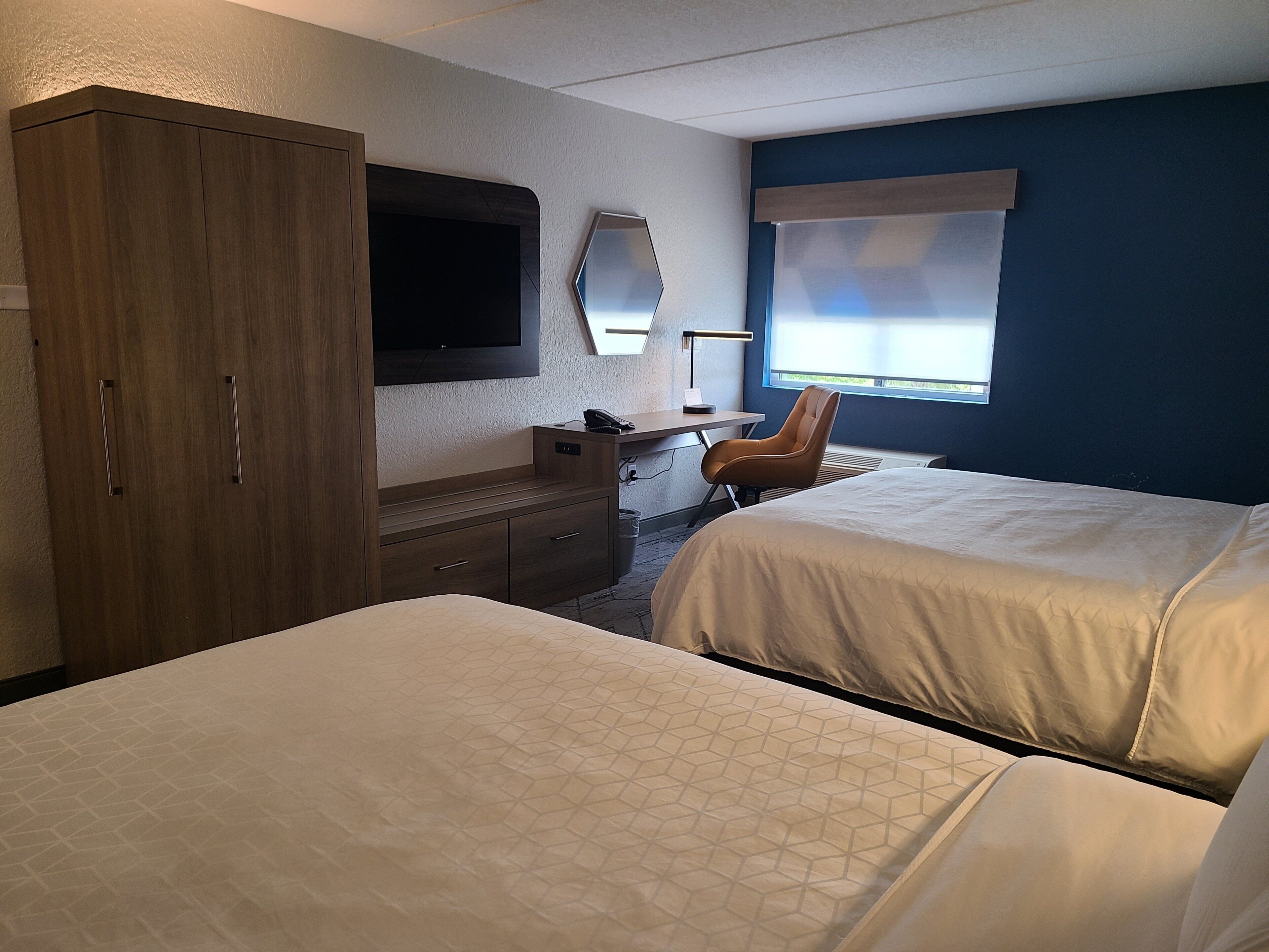 A hotel room with two beds, a desk, a chair, a wardrobe, and a television.