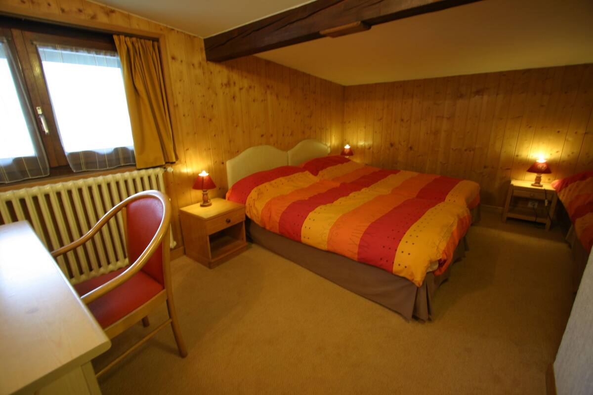 A cozy room with a large bed, a chair, a small table, and a window with curtains.