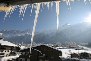 Eine Berghütte mit Holzhäuschen, schneebedeckten Dächern und Blick auf schneebedeckte Berge.