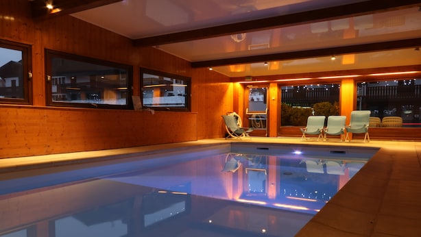 An indoor swimming pool with wooden walls and a view of the outside at night. - Hôtel Chris-tal (Les Houches)