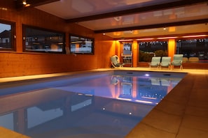 Una piscina interior con paredes de madera y vistas al exterior de noche.