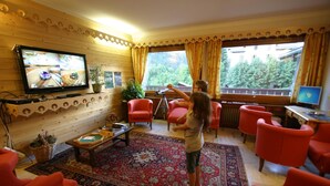 A cozy living room with a television, red chairs, a large rug, and a window with curtains. - Hôtel Chris-tal (Les Houches)