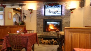 A cozy restaurant with a stone fireplace, wooden furniture, and a television displaying a deer. - Hôtel Chris-tal (Les Houches)