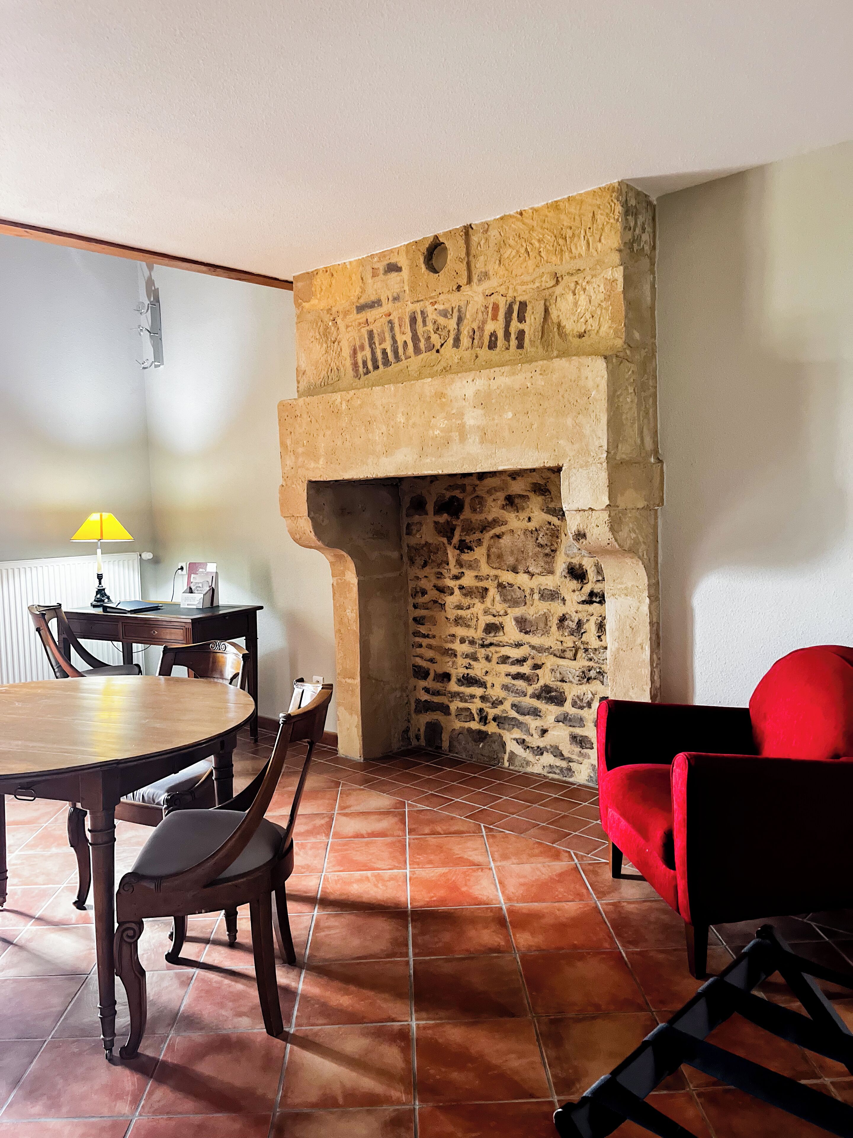 A dining area with a stone fireplace, wooden table and chairs, and a red sofa.