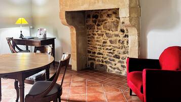 A dining area with a stone fireplace, wooden table and chairs, and a red sofa.