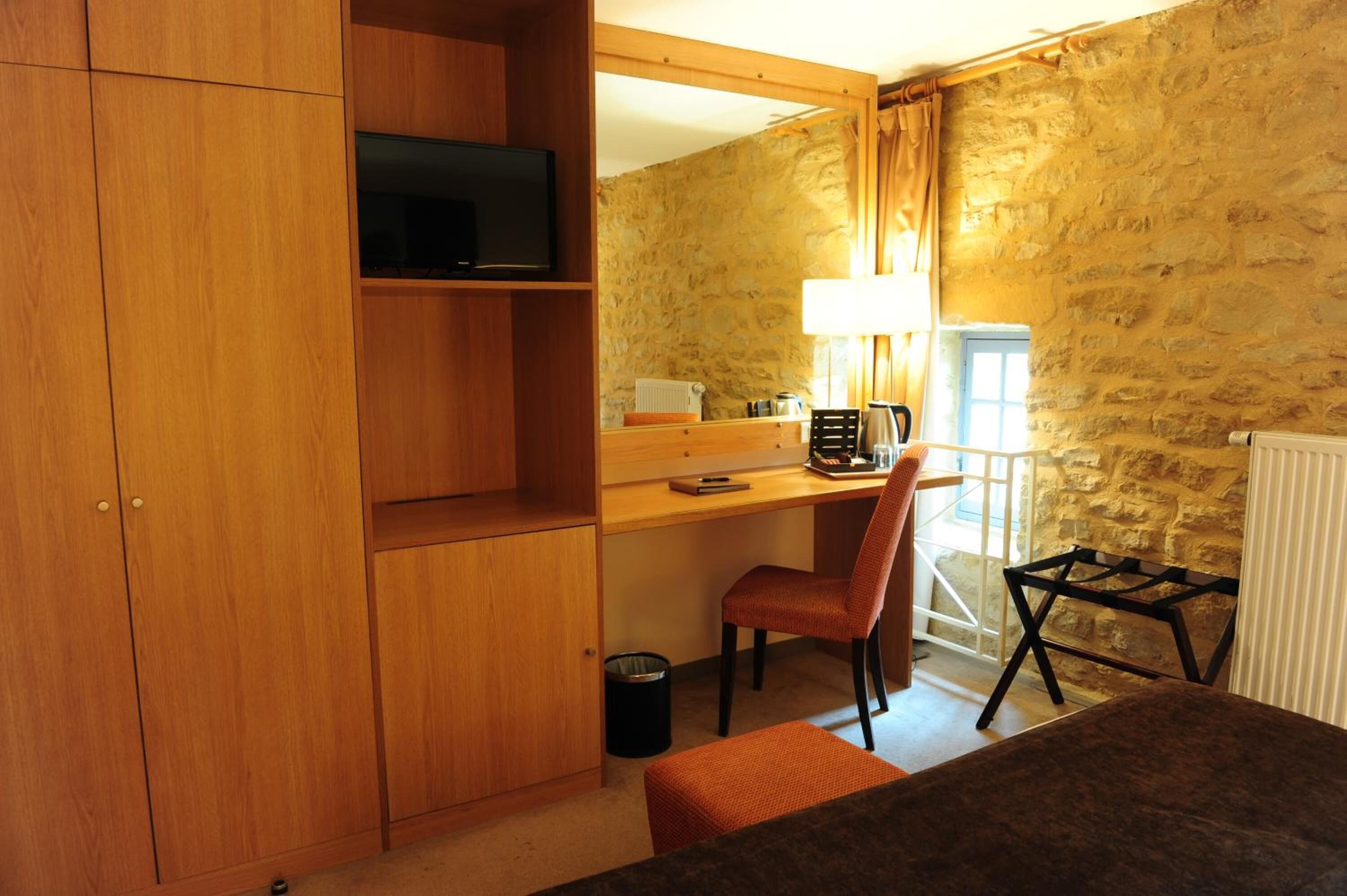 A room with a wooden desk, chair, and a television on a shelf.
