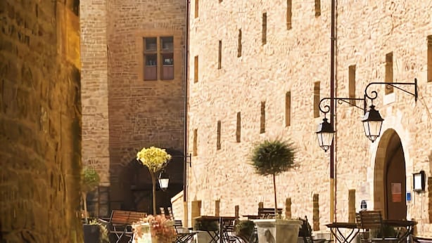 A stone building with a large arched doorway, a tiled roof, and a small balcony. - Hotel Le Château Fort (Sedan)