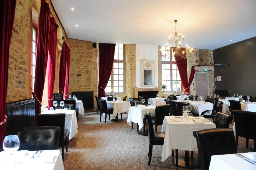 A restaurant with multiple tables set for dining, stone walls, and red curtains.