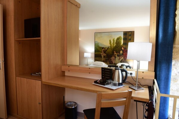 Habitación de hotel compacta con escritorio de madera, una silla, un pequeño bote de basura, un cuadro en la pared y una lámpara.