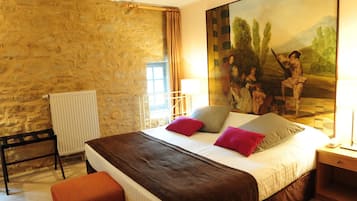 A bedroom with a stone wall, a bed with a brown headboard, a large painting, and a window with curtains.