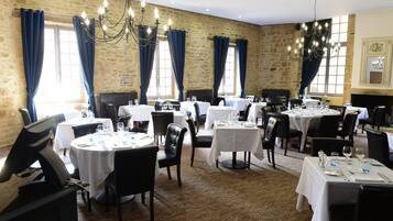 Un restaurant amb diverses taules rodones, cadires negres i cortines blaves.