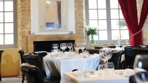 A dining area with tables set for service, a chandelier, and large windows with red curtains. - Hotel Le Château Fort (Sedan)