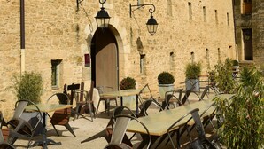 An outdoor seating area with tables and chairs in front of a stone building with multiple windows. - Hotel Le Château Fort (Sedan)