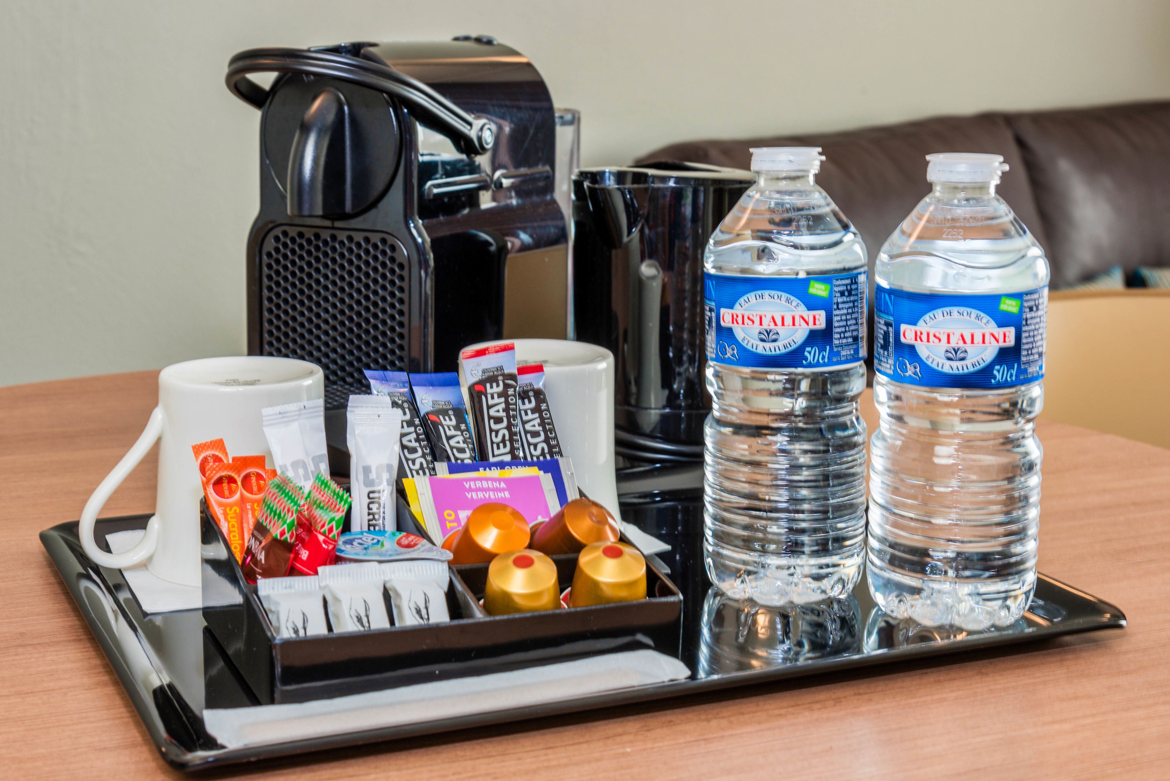 A tray with a coffee maker, two bottles of Cristaline water, a white mug, and various toiletries.