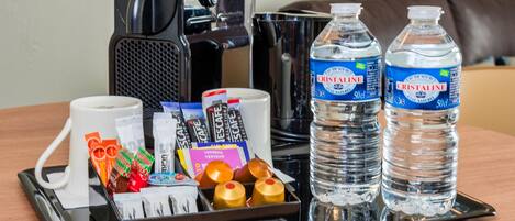 A tray with a coffee maker, two bottles of Cristaline water, a white mug, and various toiletries.