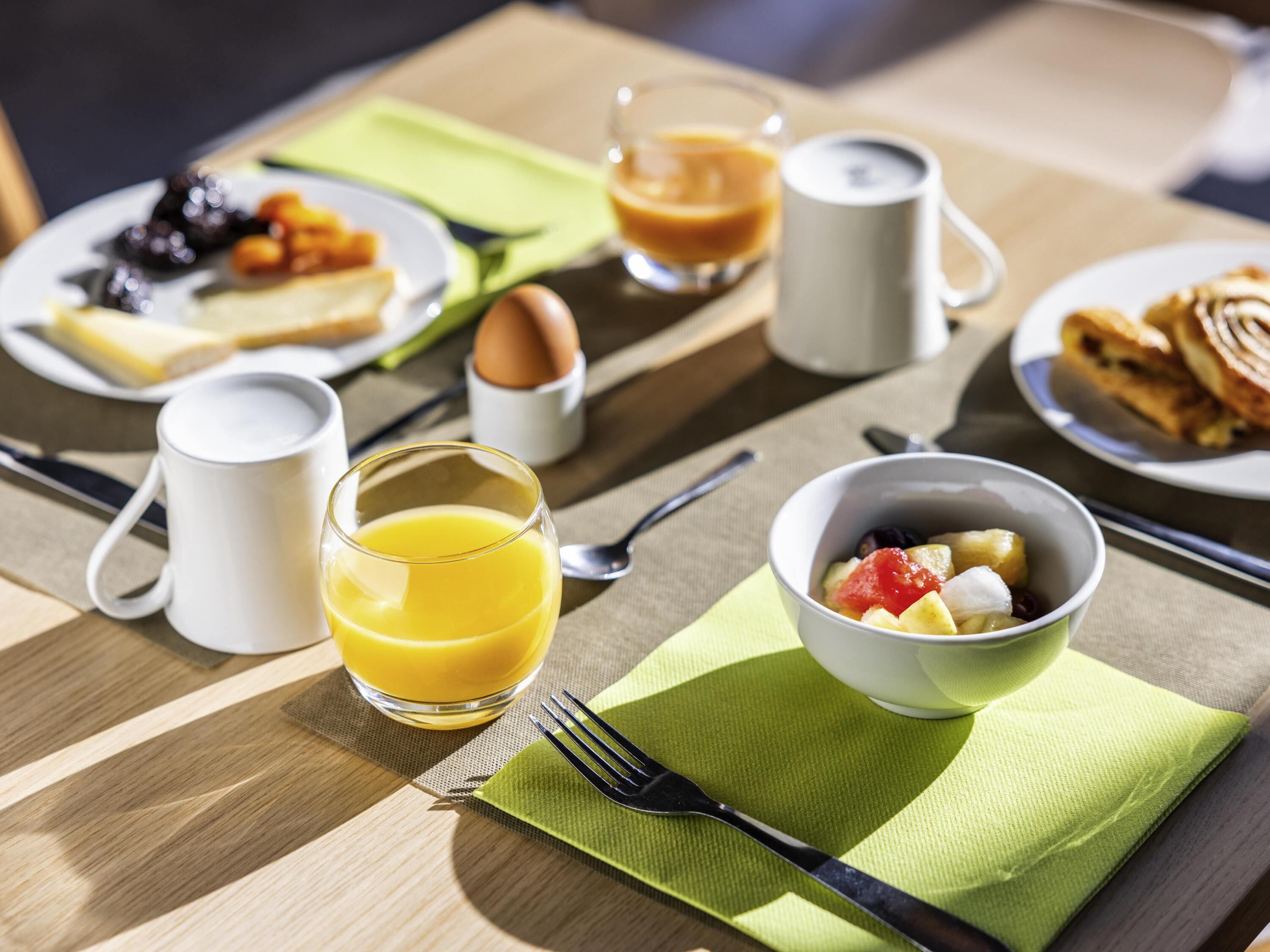 A breakfast setting with plates of food, a glass of orange juice, and a bowl of fruit.