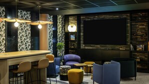 A modern bar area with a counter, bar stools, and a seating area with sofas and ottomans. - Mercure Agen Centre (Agen)