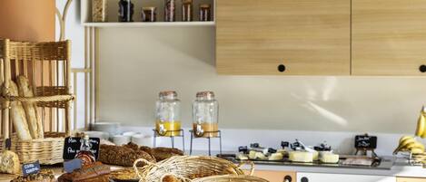 A bakery display with various breads and pastries, a wicker basket with croissants, and jars of preserves on shelves.
