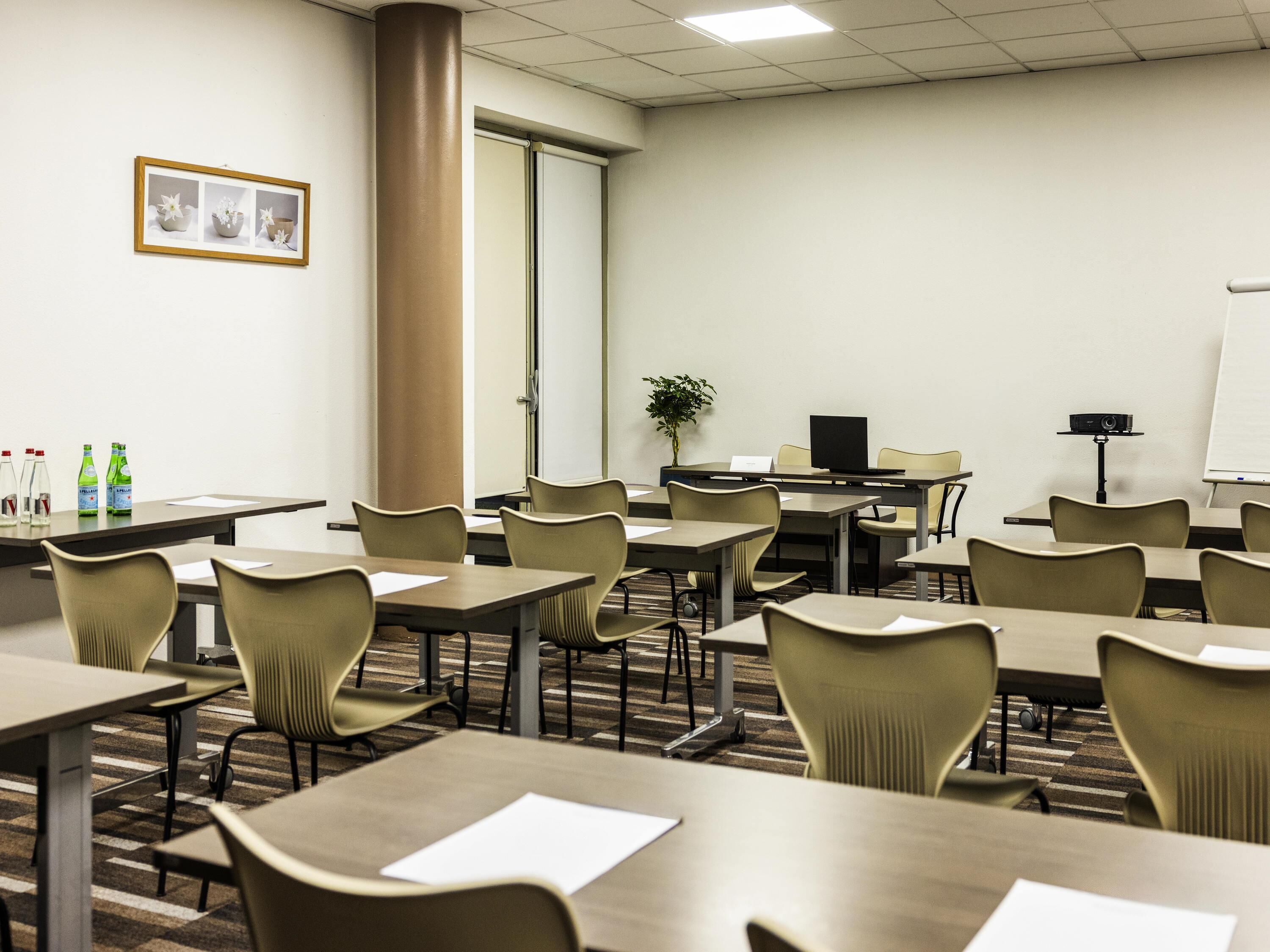 A conference room with tables, chairs, a projector, a whiteboard, and a framed picture on the wall.