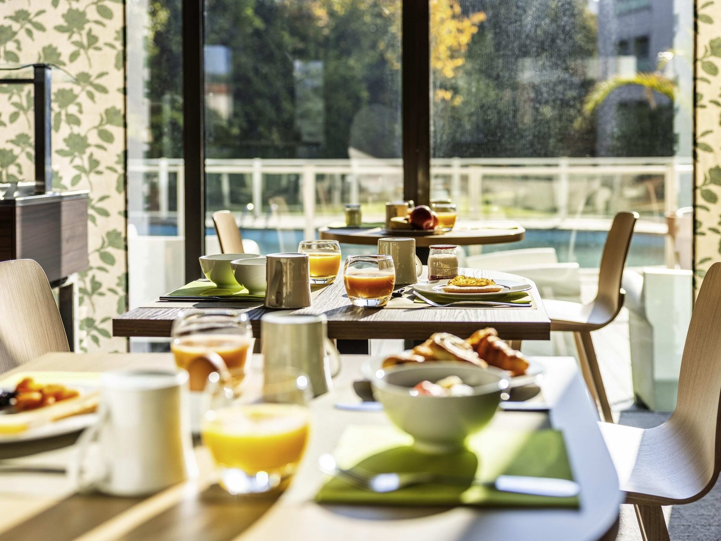A breakfast setting with tables, chairs, and a view of a pool and greenery.