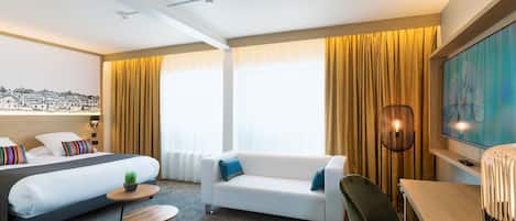 Una habitación de hotel con cama, sofá, mesa de comedor y televisión.