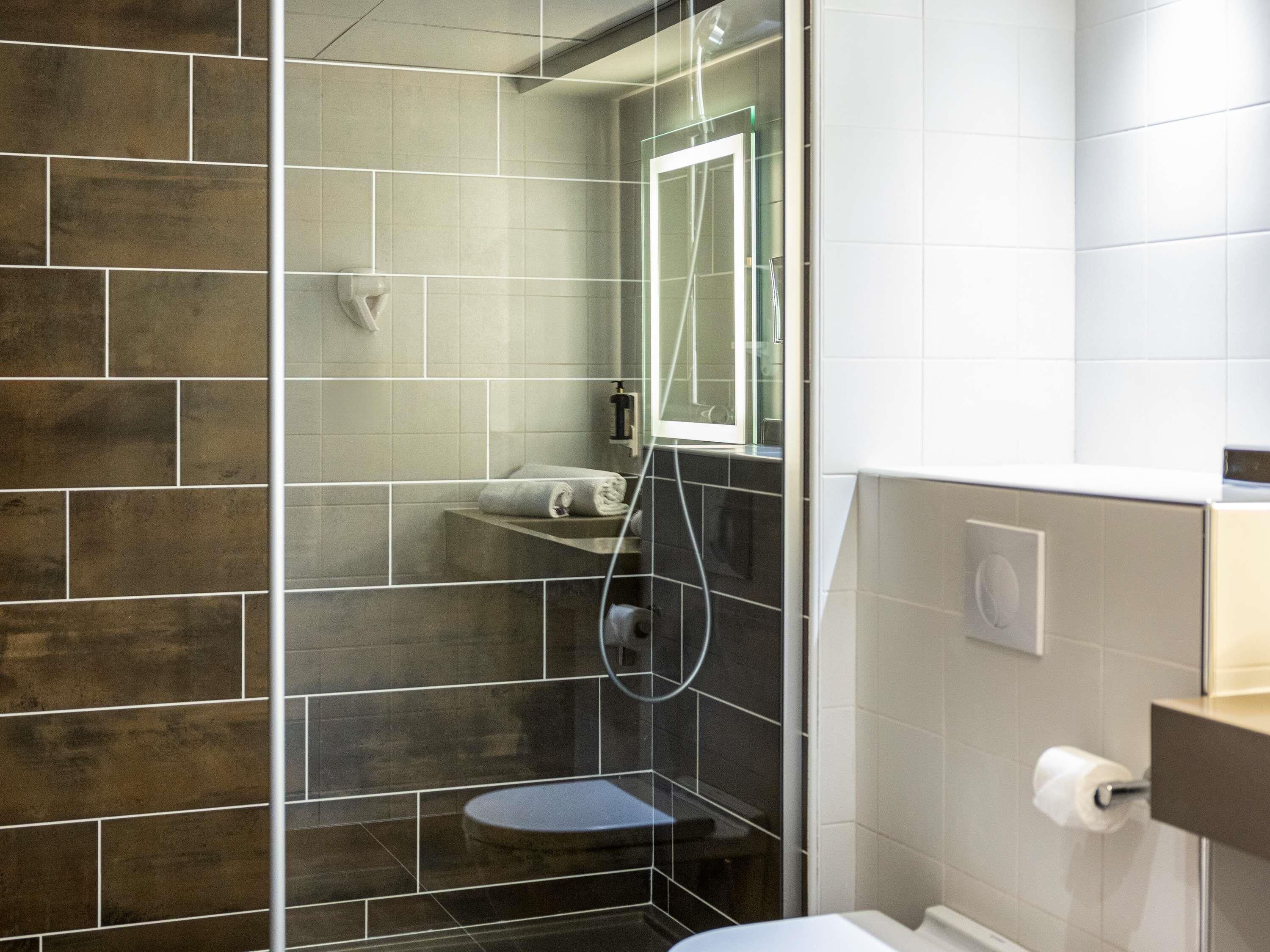 Et moderne badeværelse med glasbrusekabine, toilet og håndvask.
