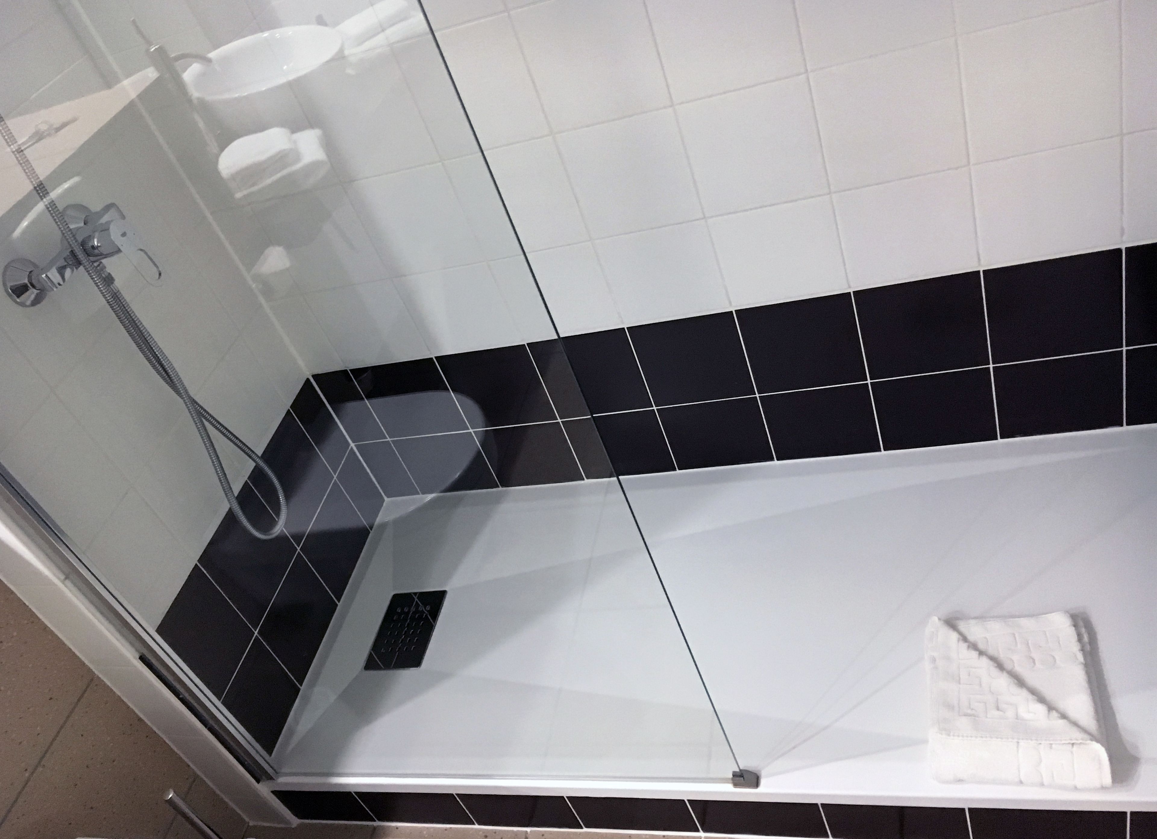 Esquina de un baño con cabina de ducha de cristal, un lavabo blanco y suelo de baldosas blanco y negro.