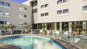 A hotel with a swimming pool, outdoor seating, and a modern building facade.