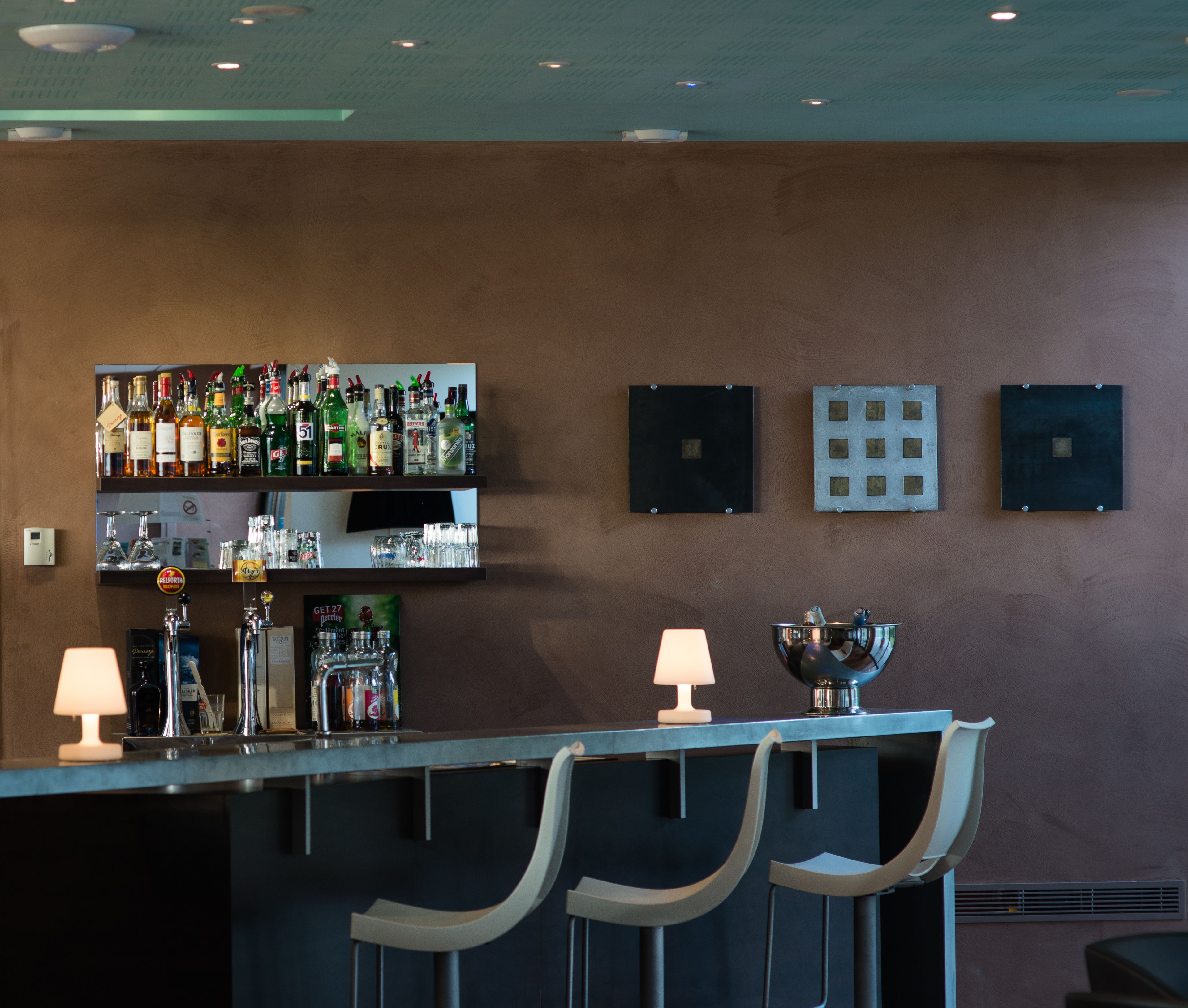 A bar area with shelves of liquor bottles, glasses, and a metal bowl on the counter.
