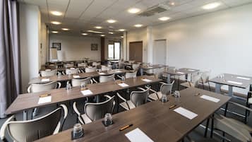 A conference room with multiple tables and chairs, equipped with water bottles and pens.