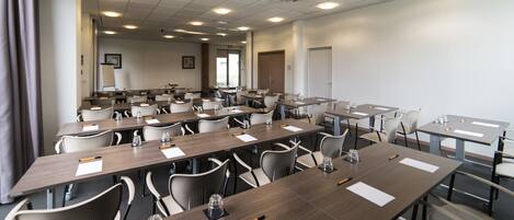Une salle de conférence dotée de plusieurs tables et chaises, ainsi que de bouteilles d’eau et de stylos.