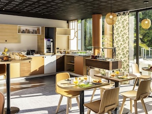 Una cocina moderna con cafetera integrada, un comedor con mesa redonda y vistas a zonas verdes a través de amplios ventanales.