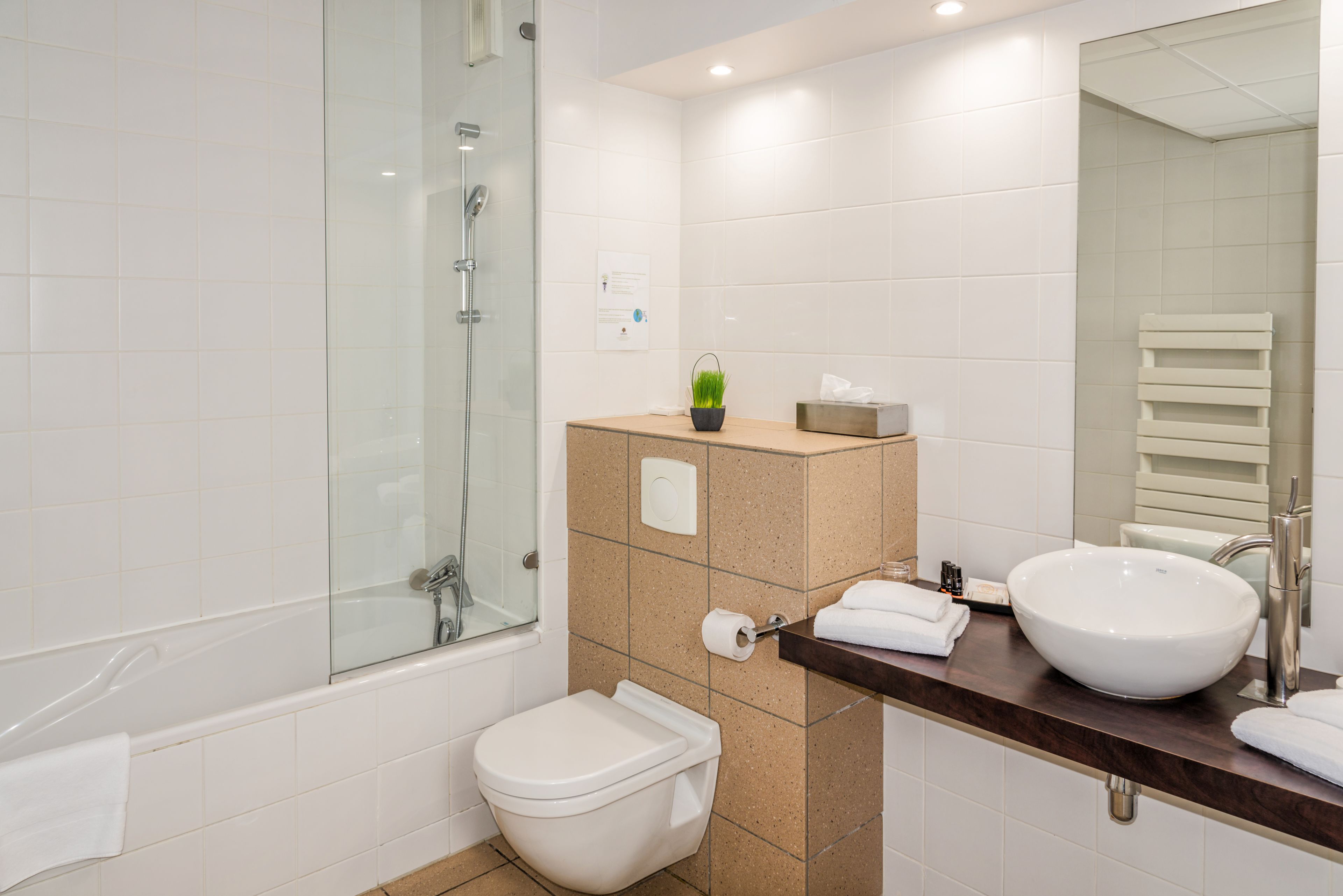 A modern bathroom with a glass-enclosed shower, a white toilet, a beige sink, and a dark wooden countertop.