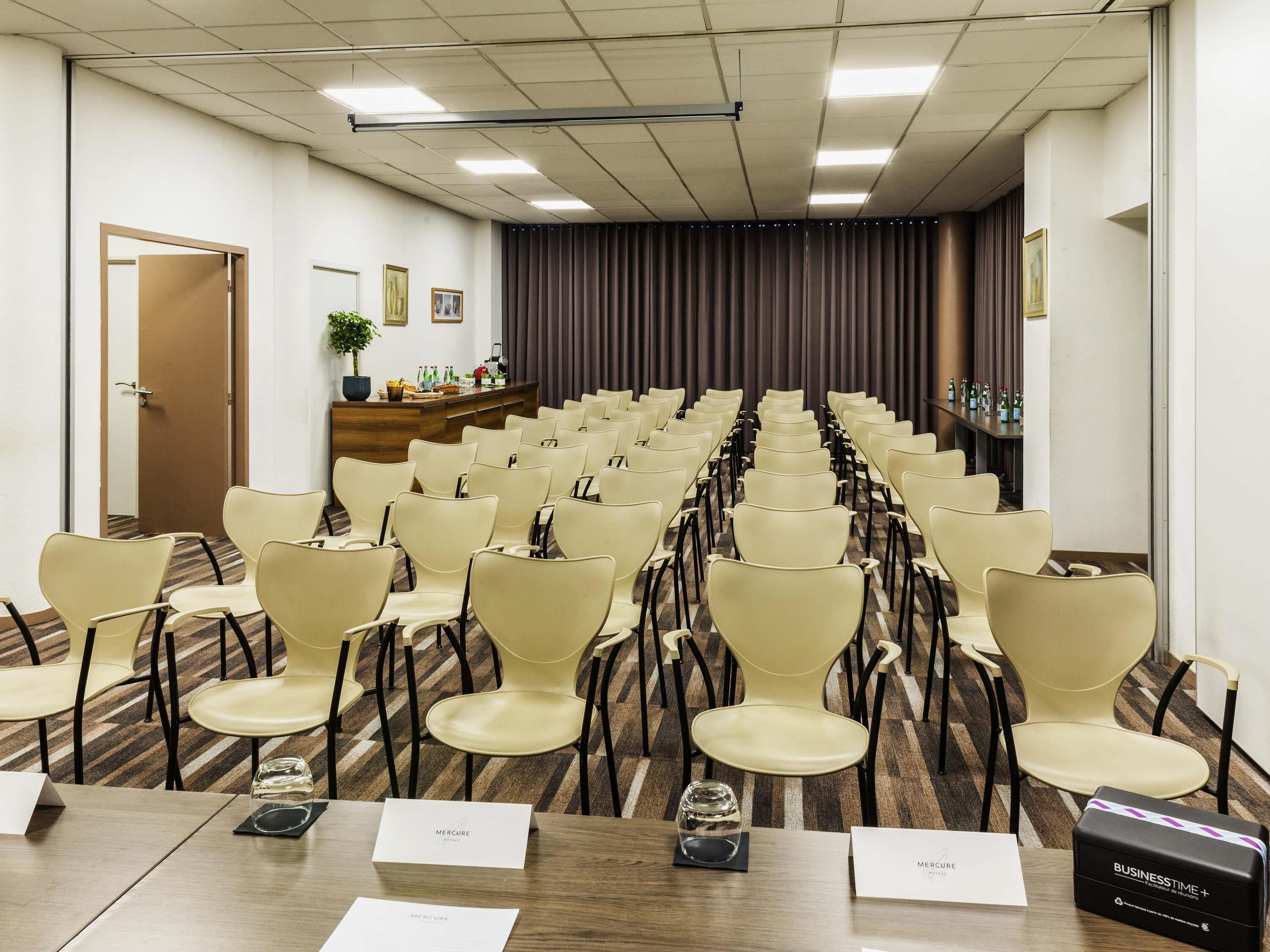 Un salón de conferencias con filas de sillas, un atril y una mesa de recepción con una planta y fotografías enmarcadas.