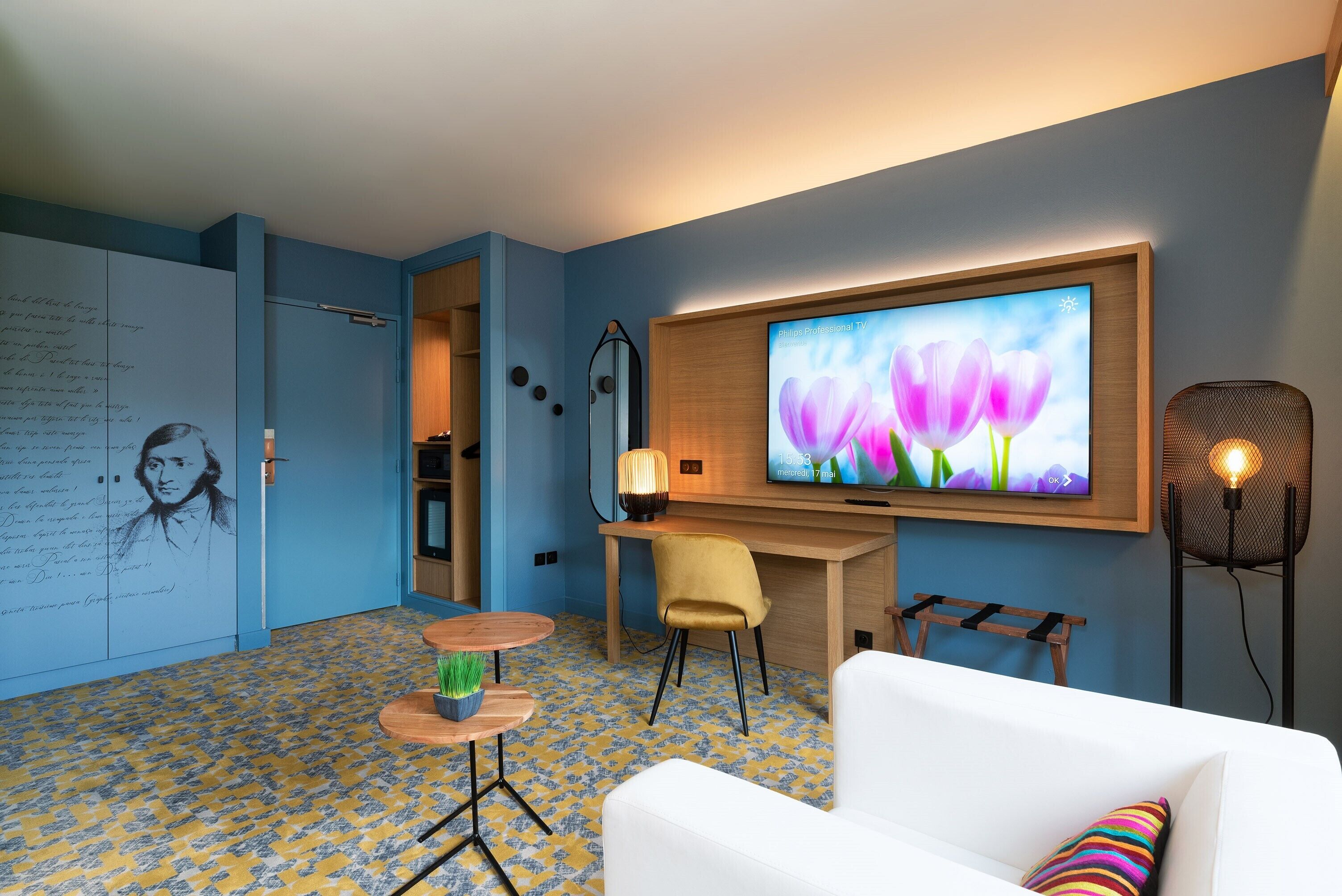 A modern room with a TV, a desk, a chair, a sofa, and a patterned floor.