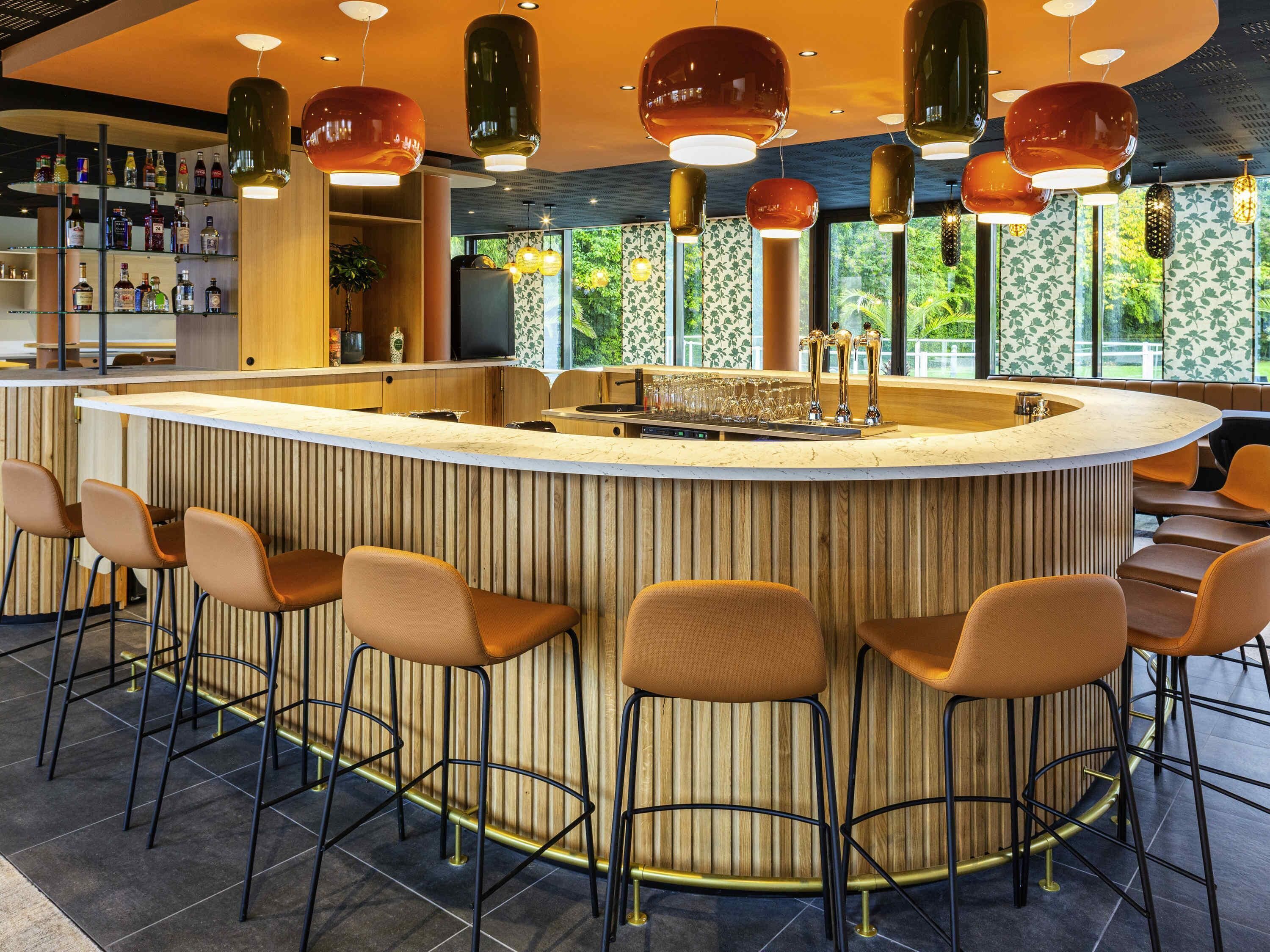 A bar area with a curved counter, multiple stools, and hanging pendant lights.