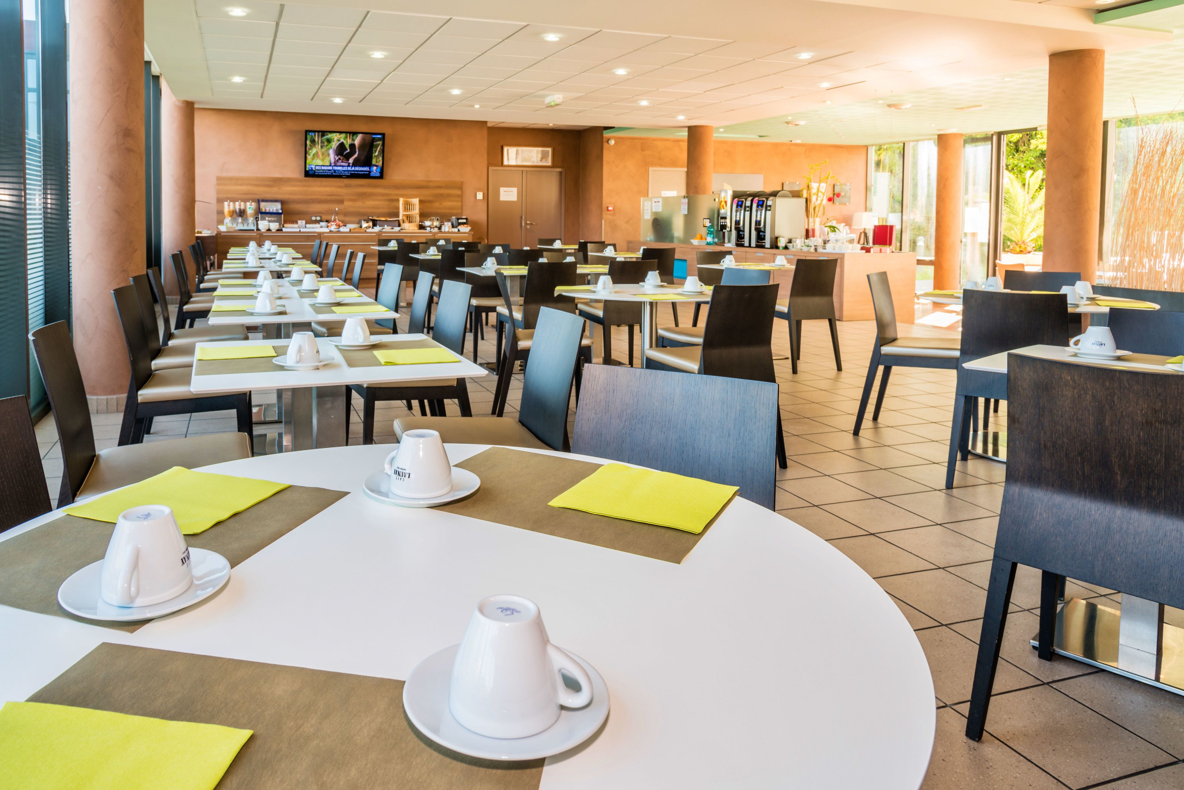 A spacious restaurant with multiple tables and chairs, a television mounted on the wall, and a counter area in the background.