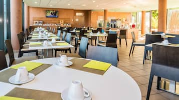 A spacious restaurant with multiple tables and chairs, a television mounted on the wall, and a counter area in the background.