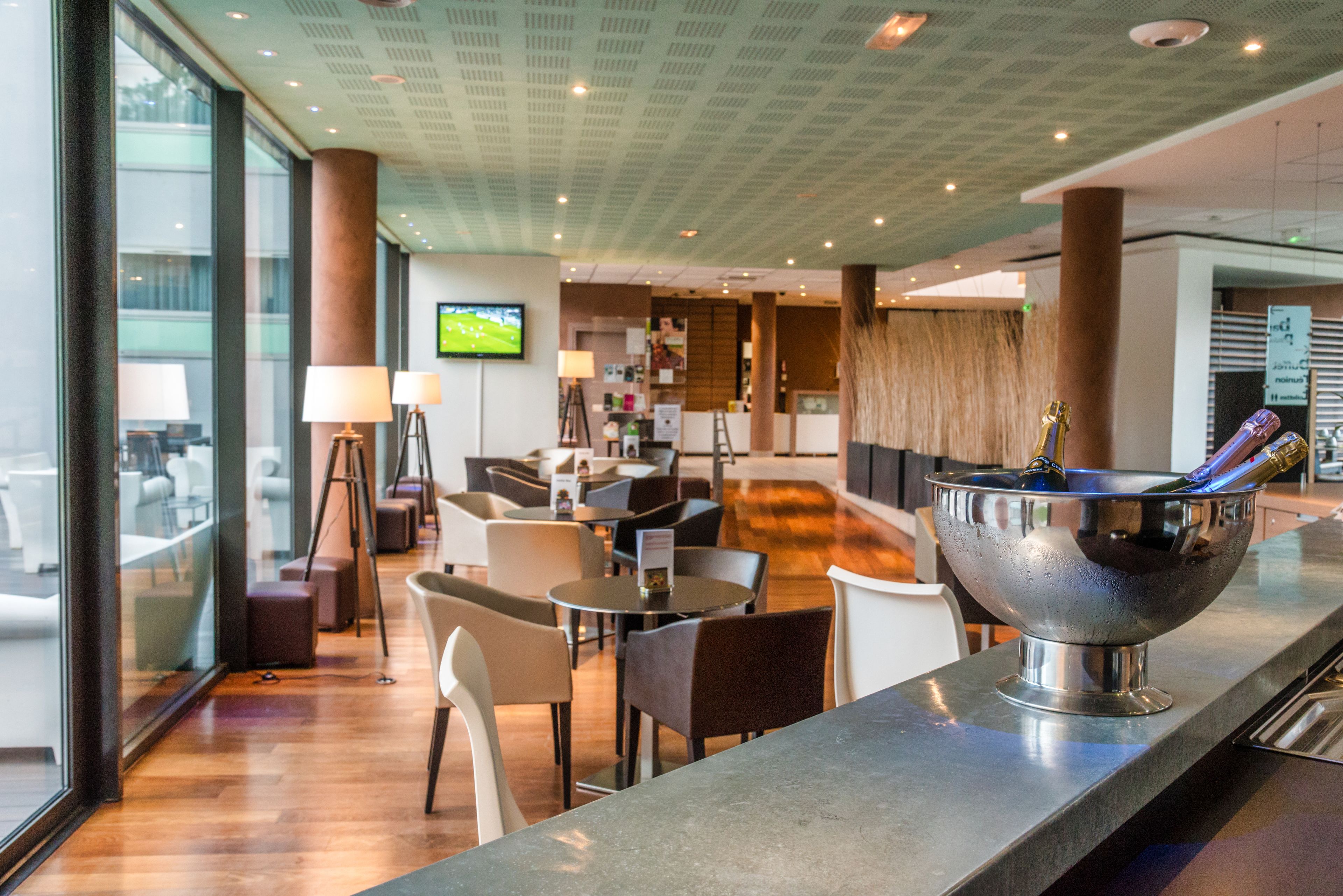 Un hall d’hôtel moderne doté d’un bar, de différents espaces de détente et d’un écran de télévision.