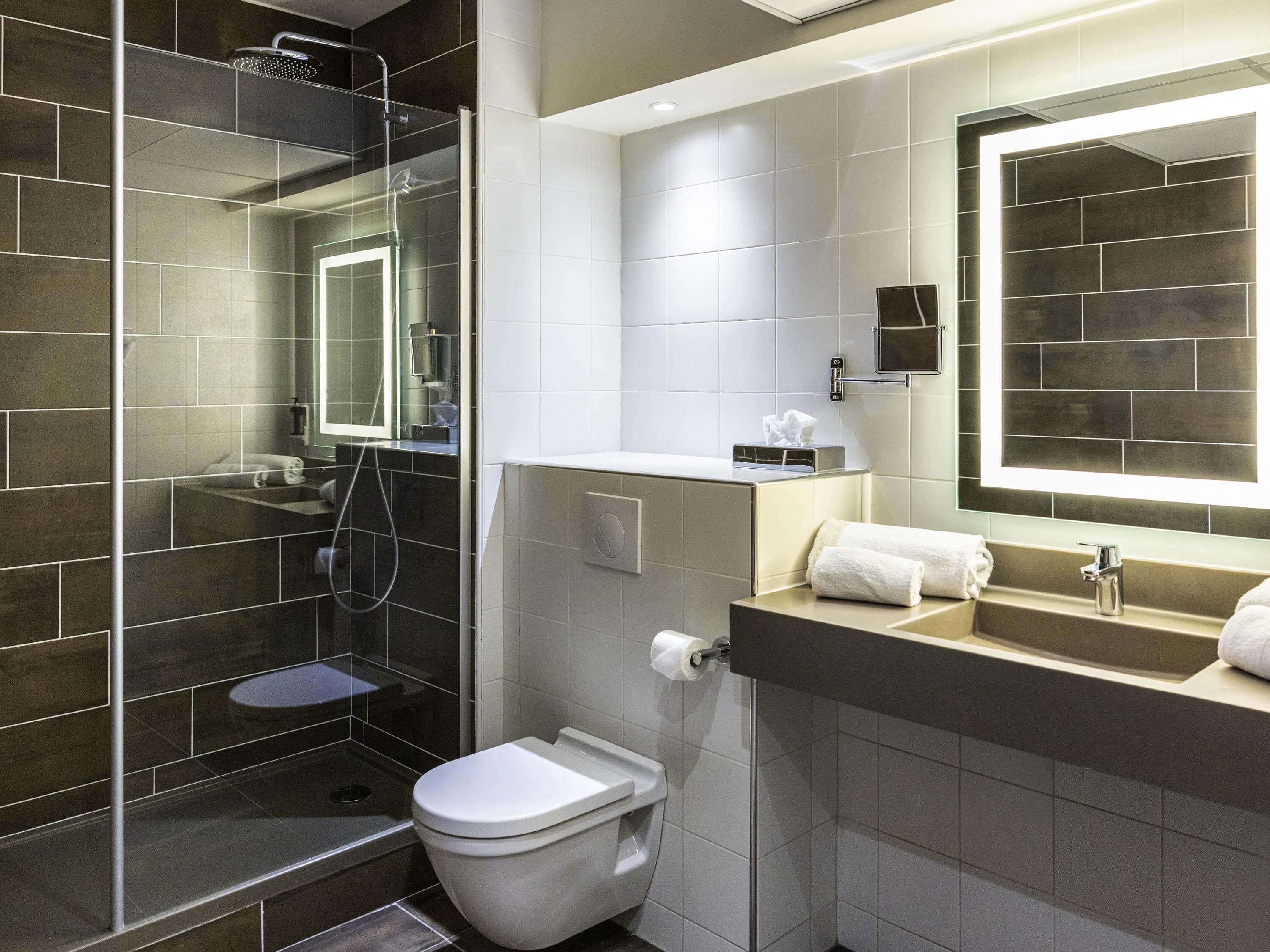 Une salle de bain moderne avec une douche à parois de verre, des toilettes, un lavabo avec un miroir et un porte-serviettes.