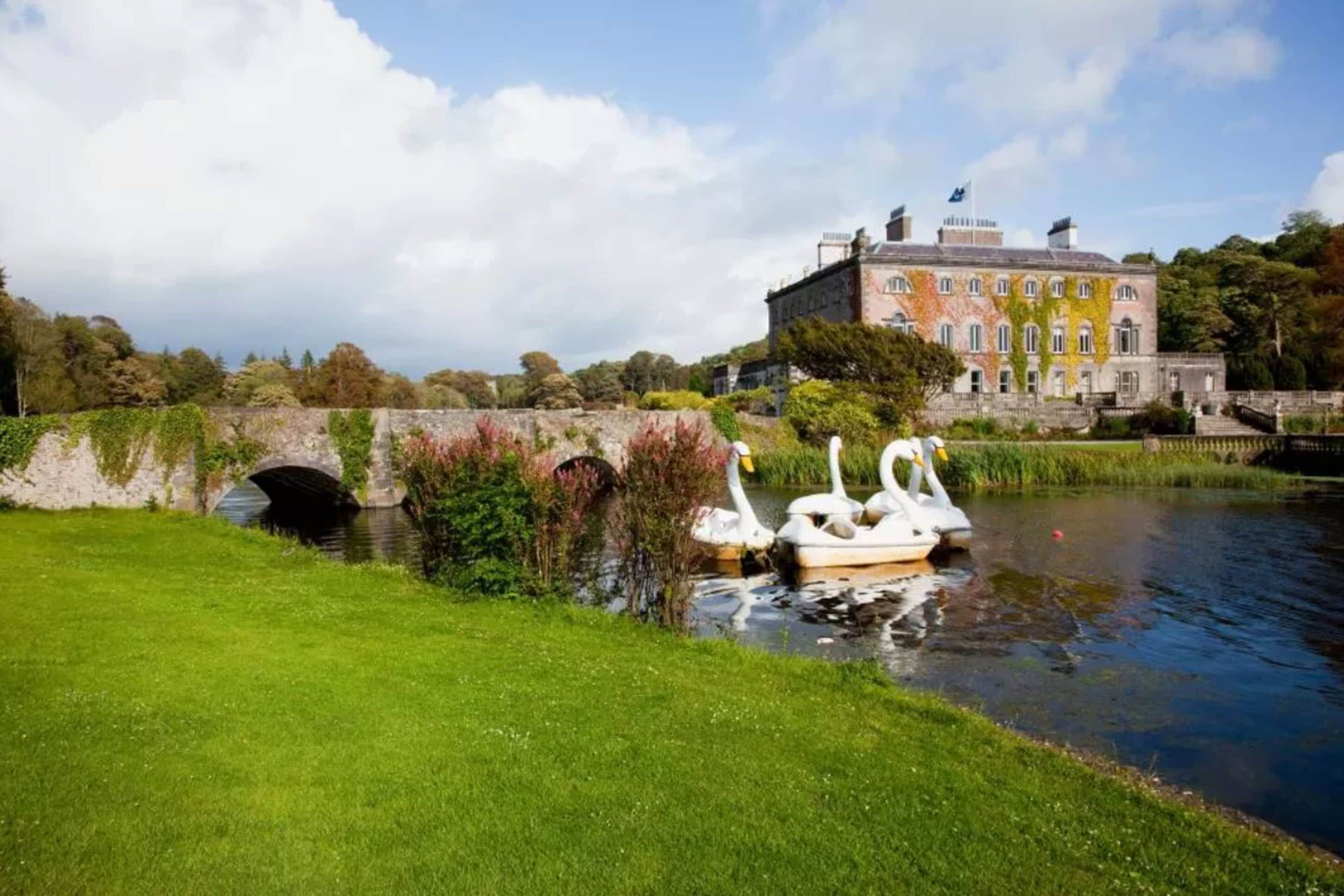A historic building with a bridge and swans by a calm water body.