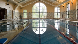 Una amplia piscina cubierta con techo alto y ventanas grandes.