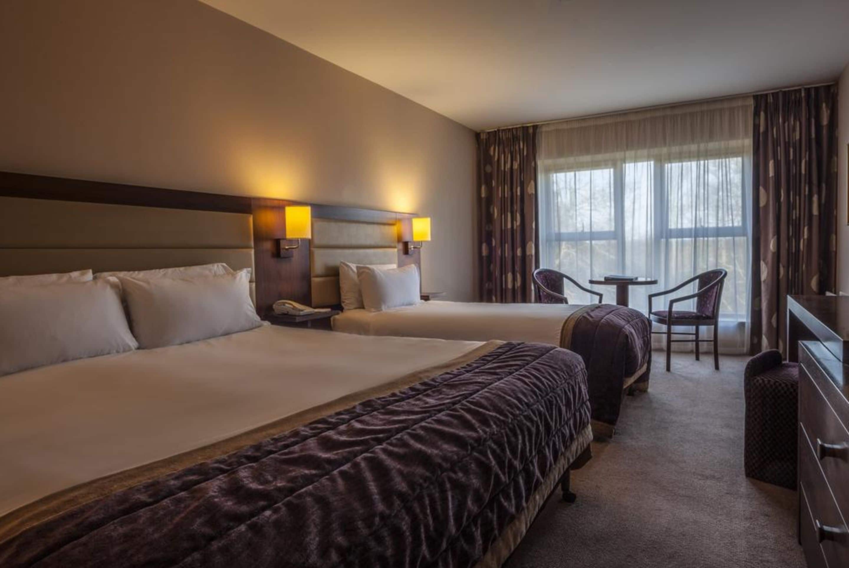 A hotel room with two beds, a small table, and a chair.