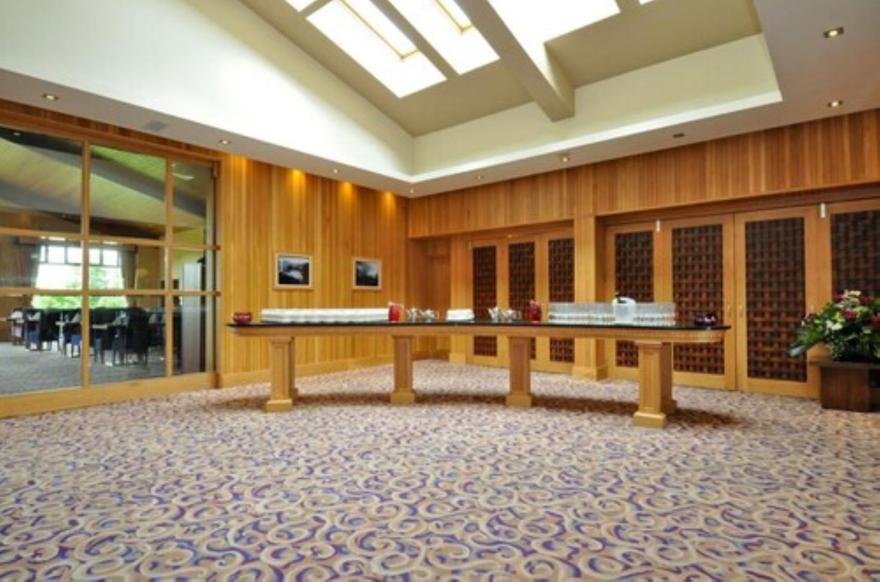A spacious room with a large table, wooden paneling, and patterned carpet.